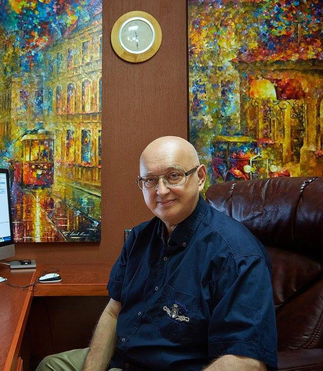 Leonid Afremov seated indoors in front of his colorful paintings
