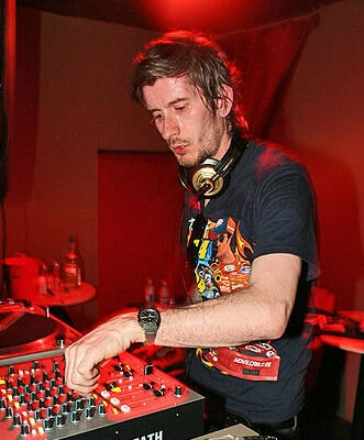 Kavinsky DJing at a mixer with headphones around his neck